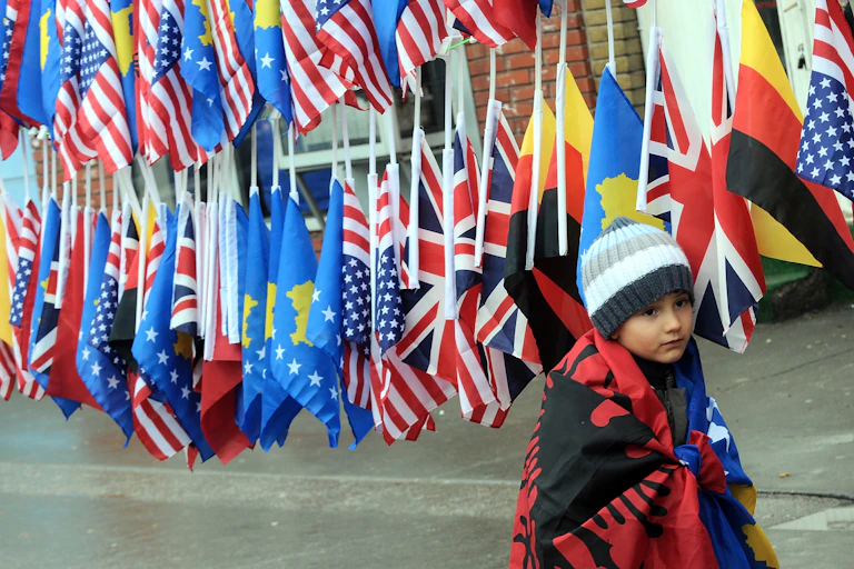 A boy wrapped in the Albanian and Kosovan flags in front of other national flags.