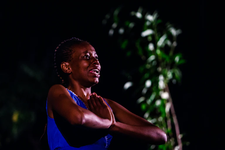 Actress on stage holds hands in prayer gesture.