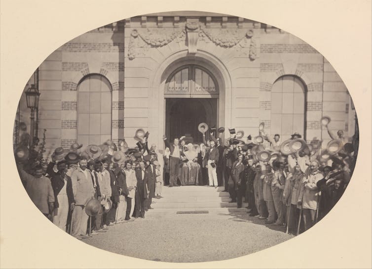 A photograph of hospital patients stood outside, raising their hats to celebrate a marble bust of Napoleon III.