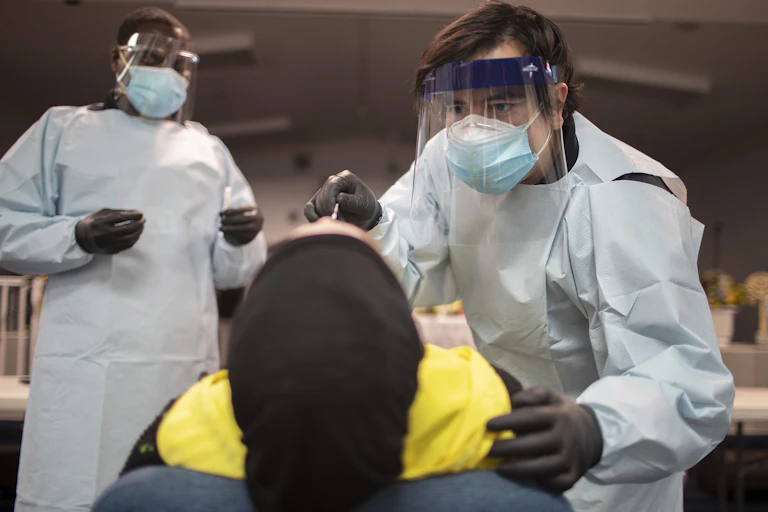 A person lying on their back is being swabbed by a healthcare worker in PPE for a COVID-19 test.