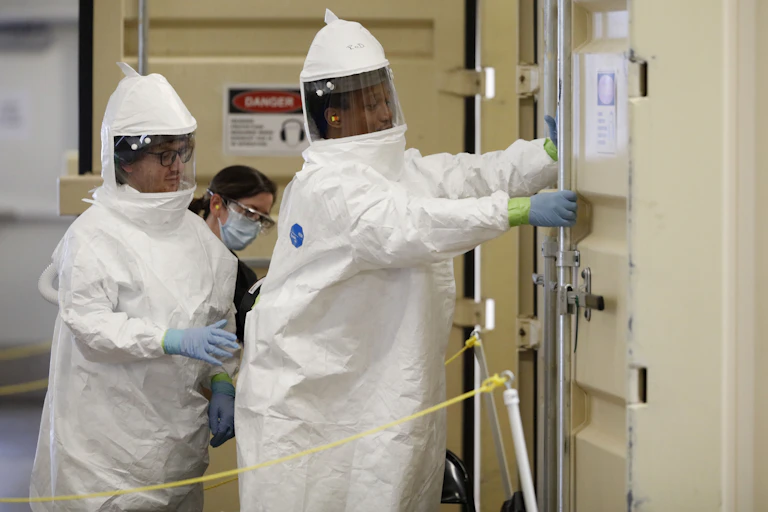 Workers wearing protective gear as they enter an N95 mask cleaning machine.