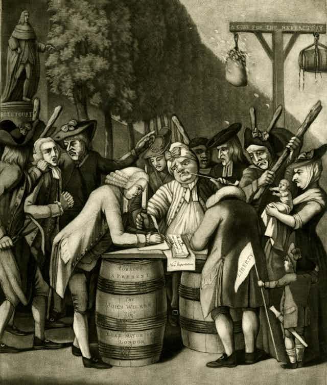 A group of people assembled around a barrel signing a document.