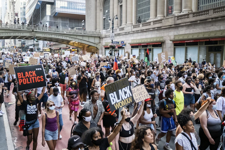 A crowd marches through New York City carrying signs.