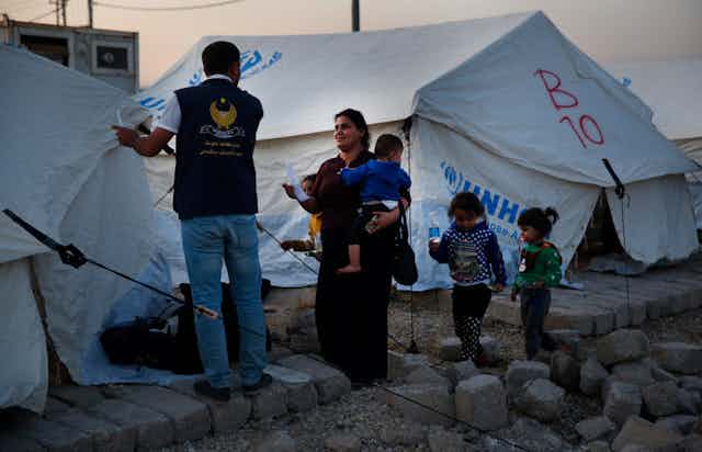 A mother with her children speaks to an aid worker in front of tents