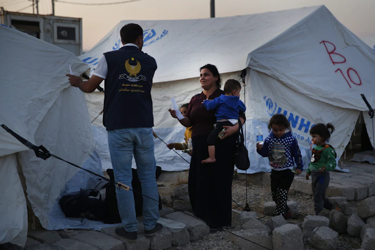 A mother with her children speaks to an aid worker in front of tents