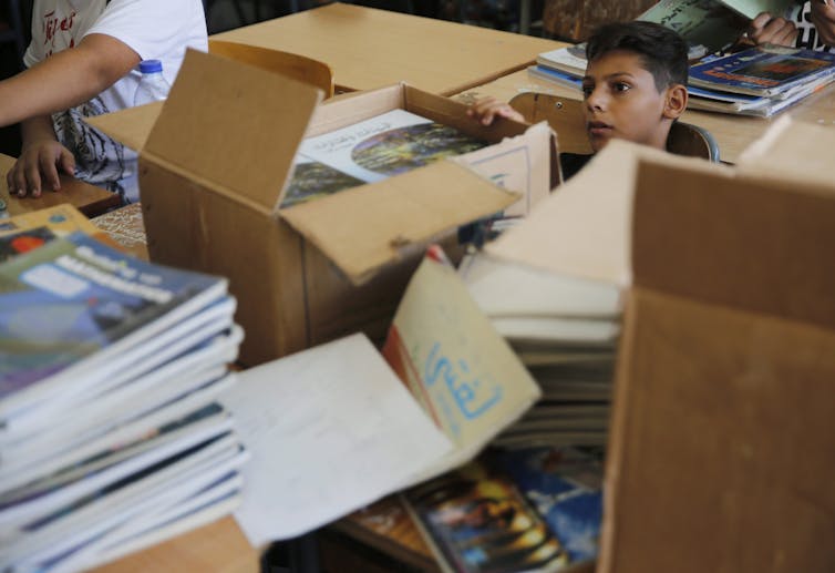 A schoolboy sits between boxes of new books in a classroom
