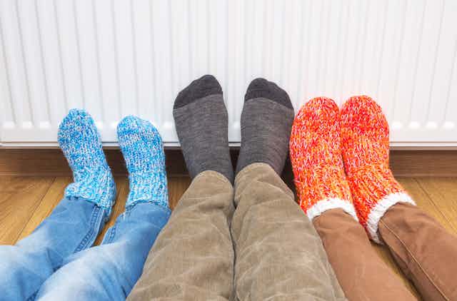 Three feet in woolly socks are against a heater keeping warm.