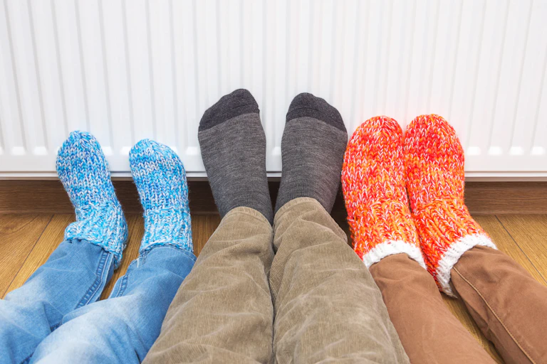 Three feet in woolly socks are against a heater keeping warm.