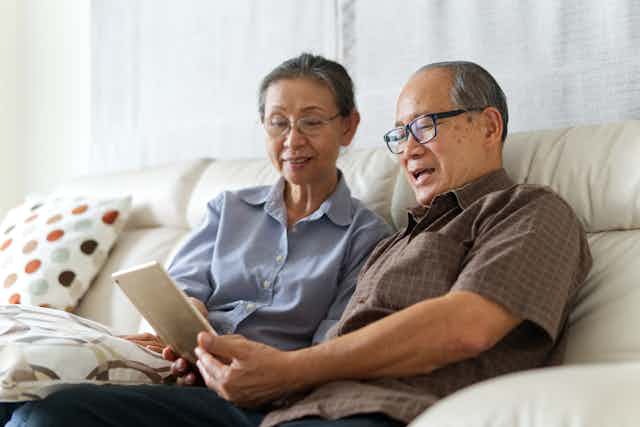 Older Asian couple sitting on the couch using tablet.