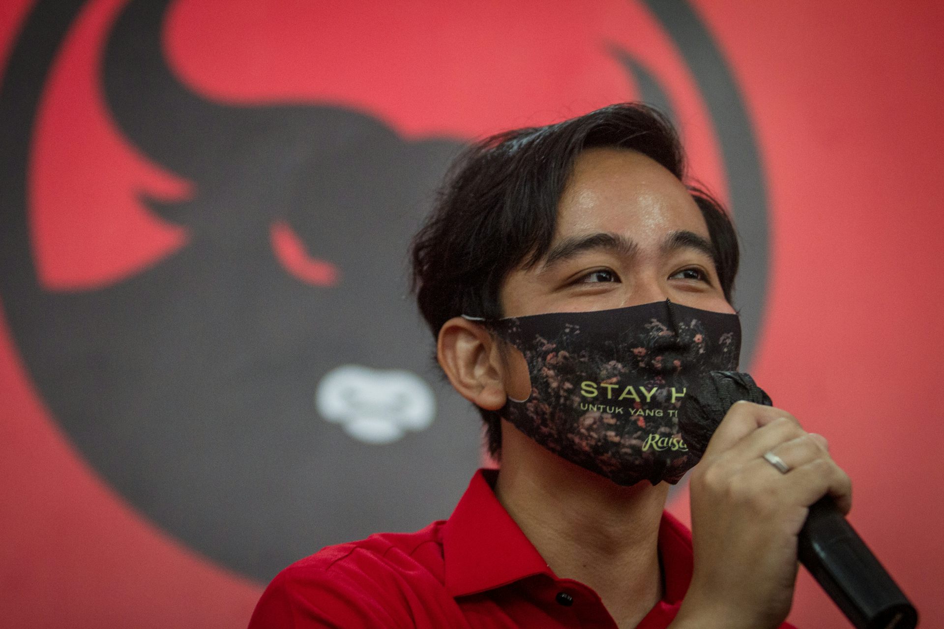Gibran Rakabuming Raka memegang mik dan mengenakan masker.
