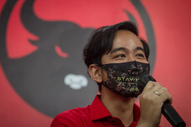 Gibran Rakabuming Raka memegang mik dan mengenakan masker.