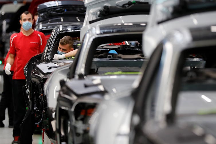 Workers wear protective face masks in an electric car production line.