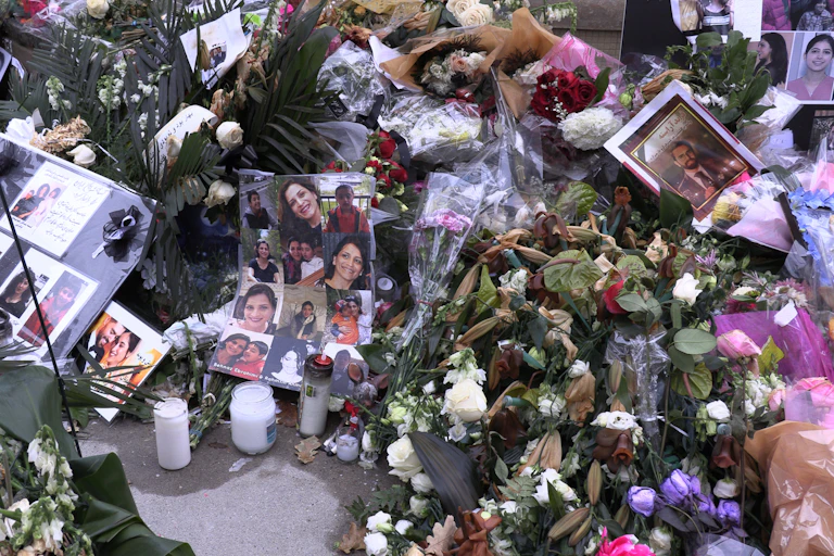 A memorial comprising photos of victims, flowers and candles on a pavement.