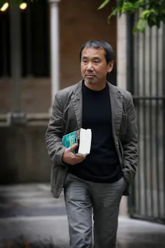 Japanese novelist Haruki Murakami walking holding a book.