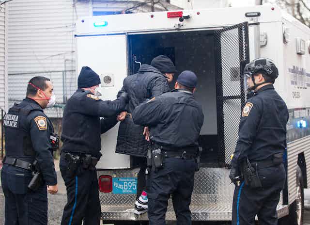 Police help a handcuffed person into the back of a police vehicle.
