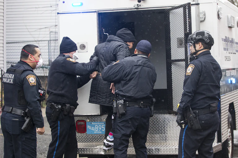 Police help a handcuffed person into the back of a police vehicle.