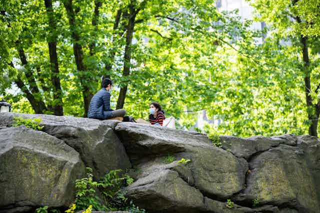 Man and woman wearing masks, sitting on rocks in Central Park, New York, NY