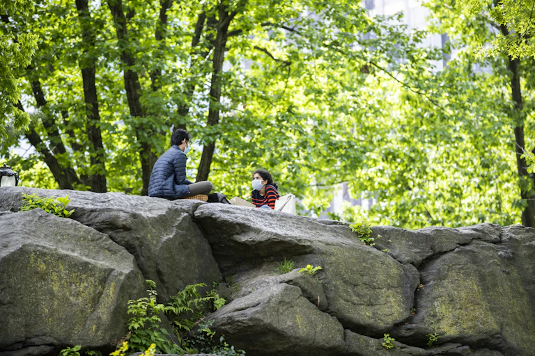 Man and woman wearing masks, sitting on rocks in Central Park, New York, NY