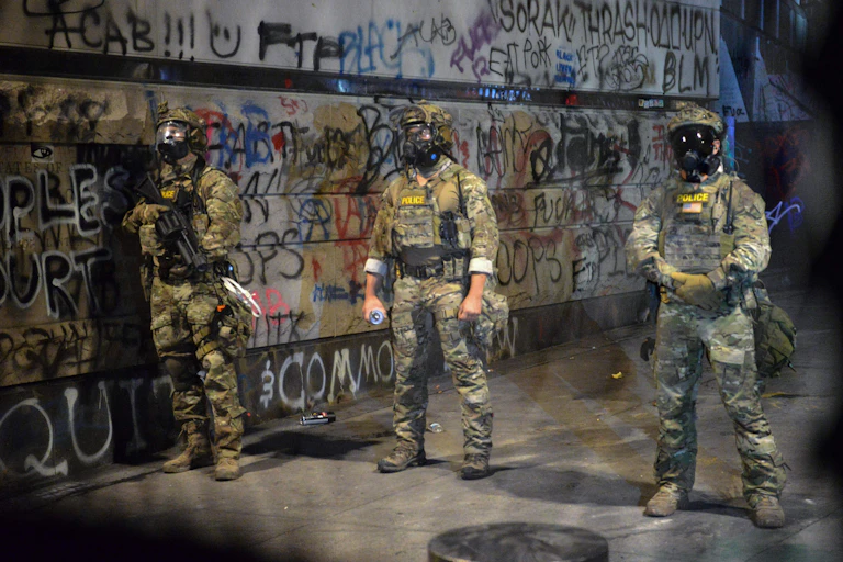 Armed federal officers stand in front of graffiti.