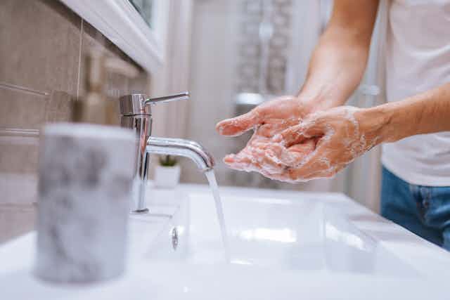 Man's hands lathered with soap at the sink, tap running.