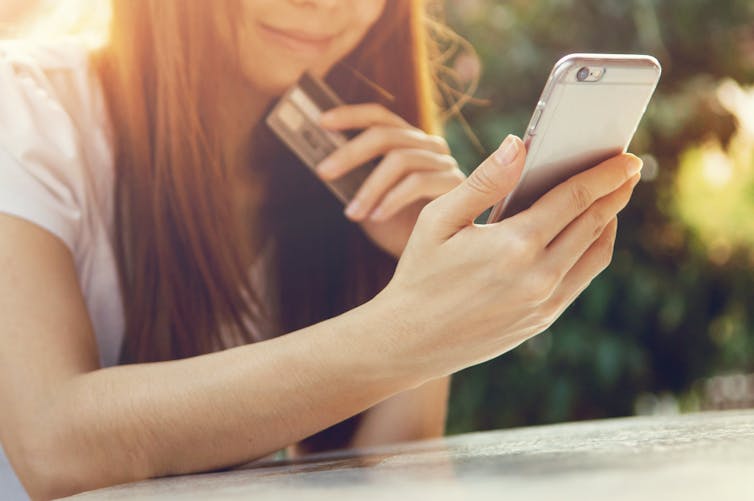 A woman looks at her phone while holding a credit card.