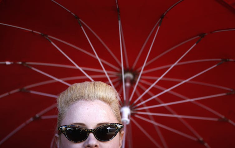 Woman wearing sunglasses under a red umbrella