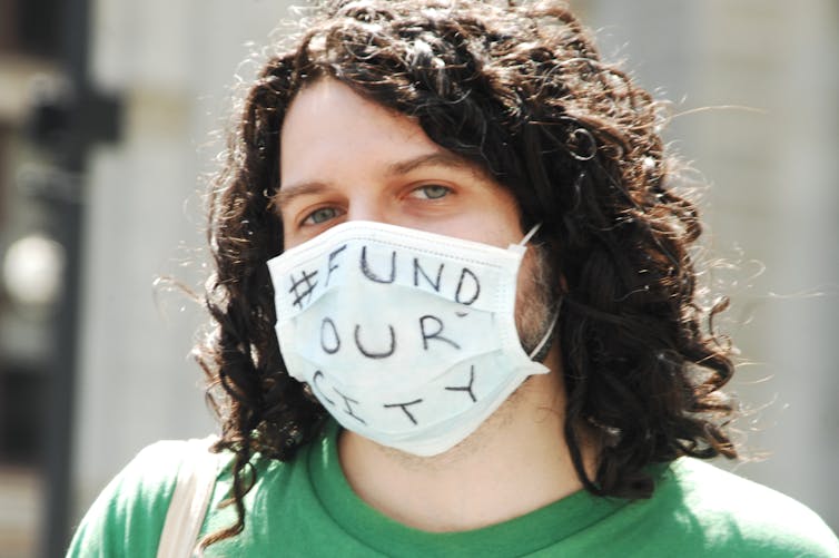A protestor wearing a mask that says 'Fund our city.'