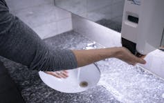 A man reaches for a soap dispenser as he washes his hands.