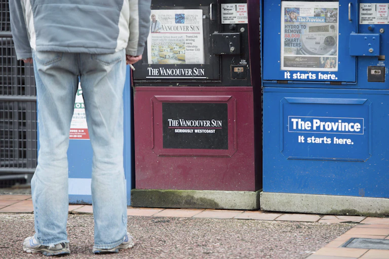 A man stands in front of newspaper boxes.