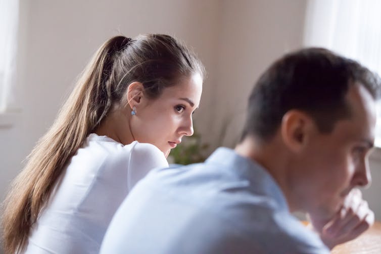 Photo from behind of a woman who appears to be offended looking over her shoulder at a man sitting next to her in an office meeting setting.