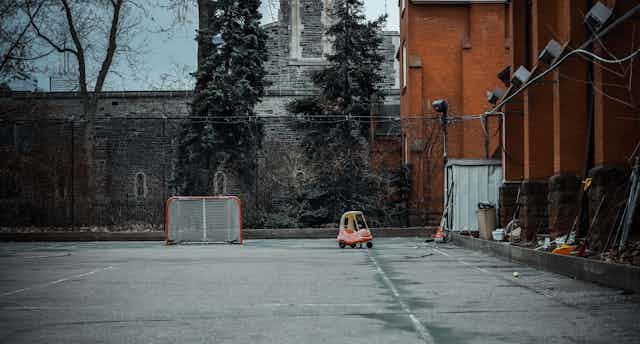 An empty schoolyard, with a hockey goal and toddler car in the background.