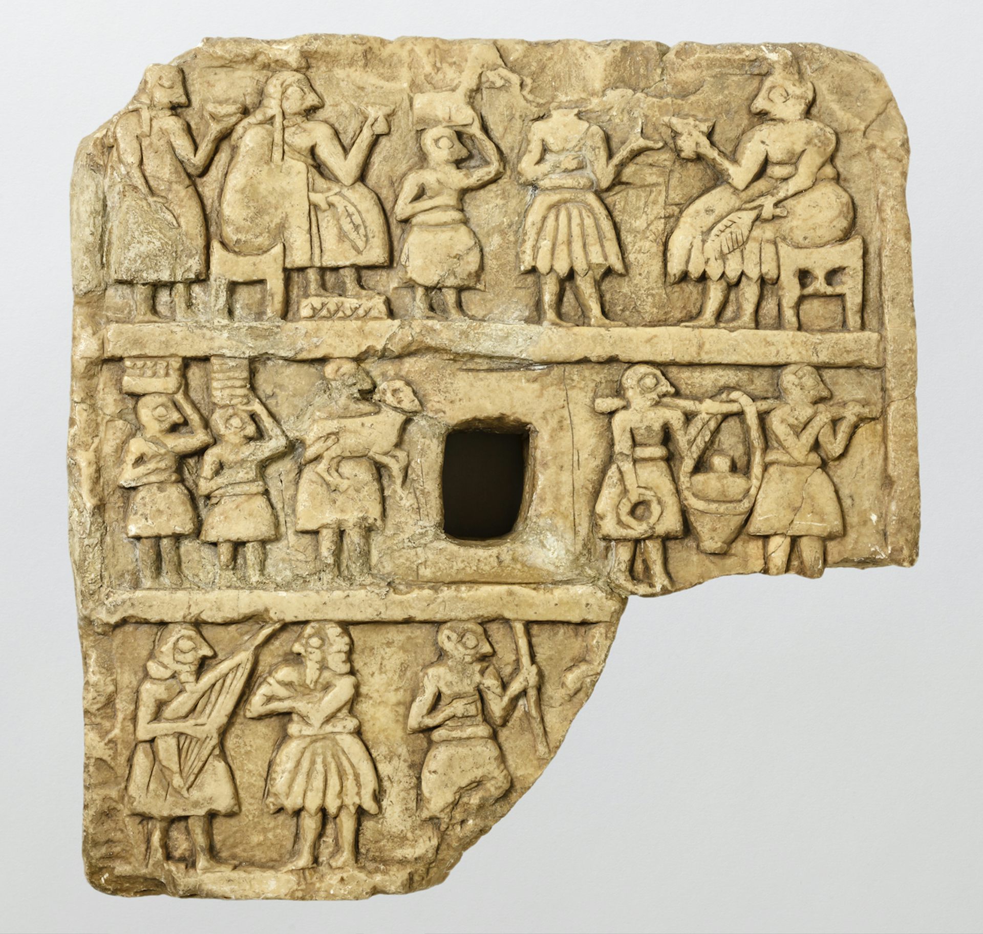 Kamienna tabliczka przedstawiająca zgromadzonych ludzi pijących z pucharów