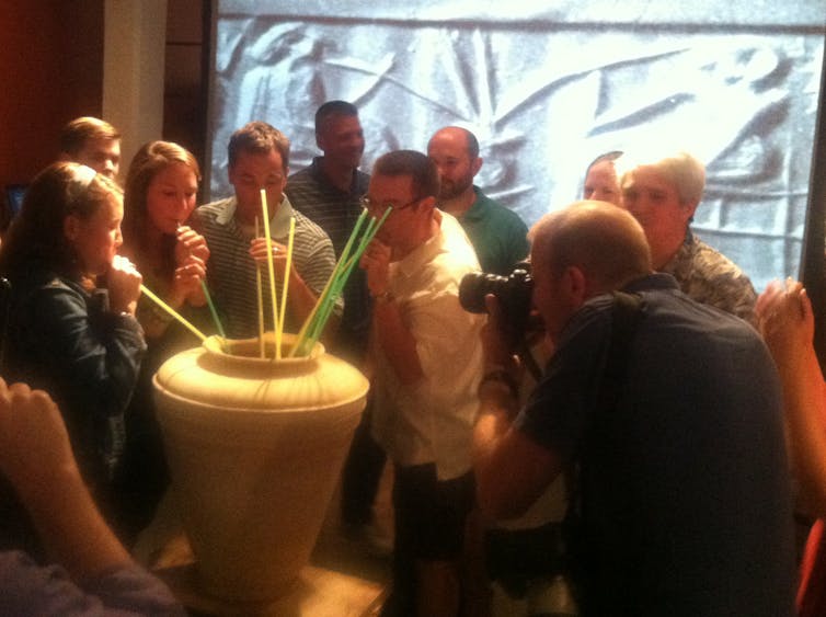 People gathered around a large vessel drinking from long straws.