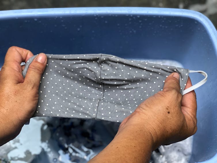 A person washing their mask in a bucket with water and detergent