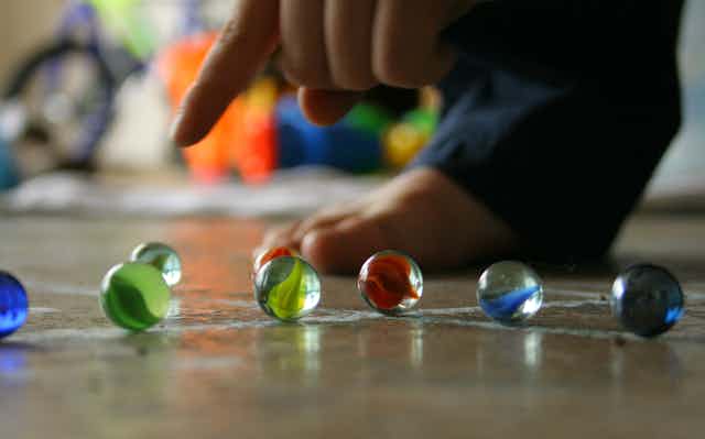 A finger pointing at several marbles on the ground.