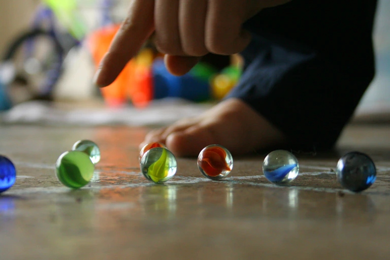 A finger pointing at several marbles on the ground.