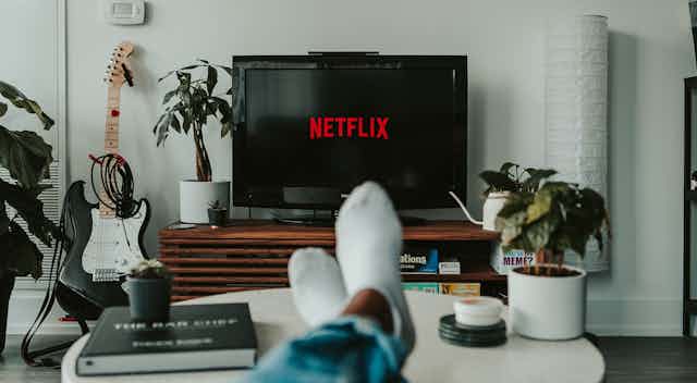 A person's feet are on a table why Netflix loads on their television screen in front of them 