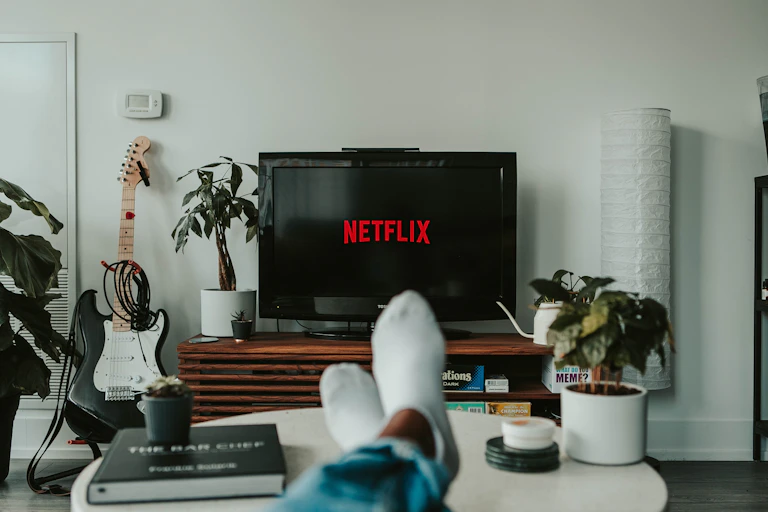 A person's feet are on a table why Netflix loads on their television screen in front of them