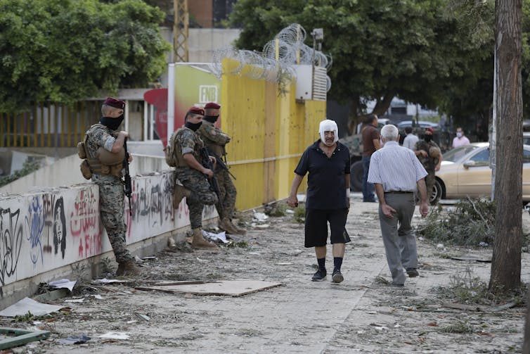 A man with bandages on his head walks past
soldiers in Beirut.