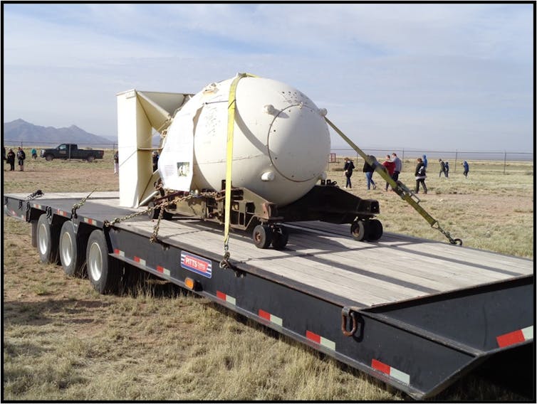 A replica of the atomic bomb being carried on a flatbed trailer.
