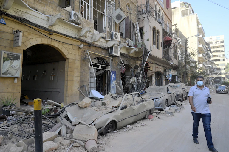 A man walks next to damaged vehicles in the aftermath of a massive explosion in Beirut, Lebanon.