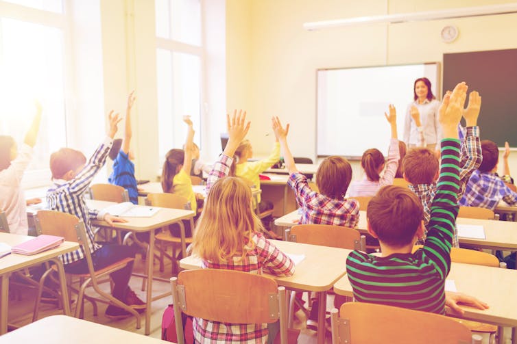 Picture of children raising their hands in the classroom.