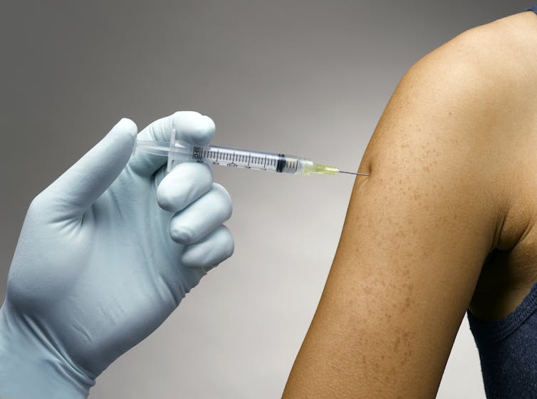 Hand injecting a shot into a bare upper arm