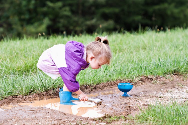 A young girl plays in the mud.