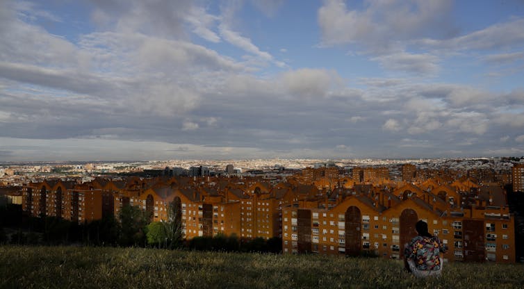 A boy sits on a hill and looks over the city.