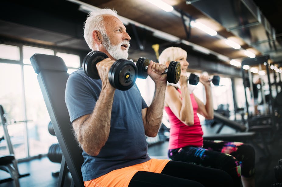 Older man and older woman lift dumbbells in the gym.