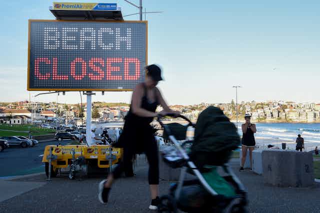 A woman with baby pushchair walks past a 'beach closed' sign.