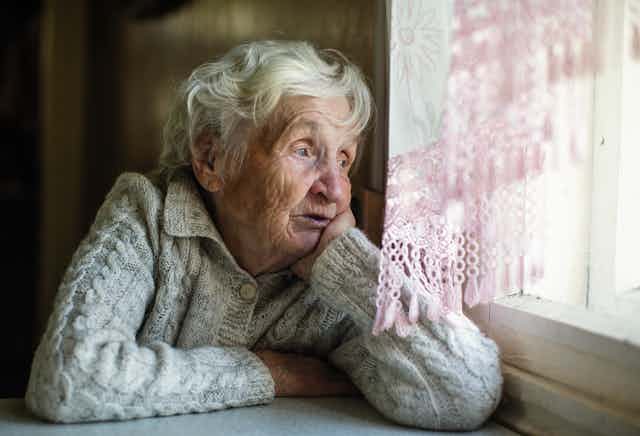 Elderly woman looks out of her window.