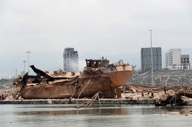 A ship's wreckage in the foreground and a devastated urban landscape in the background