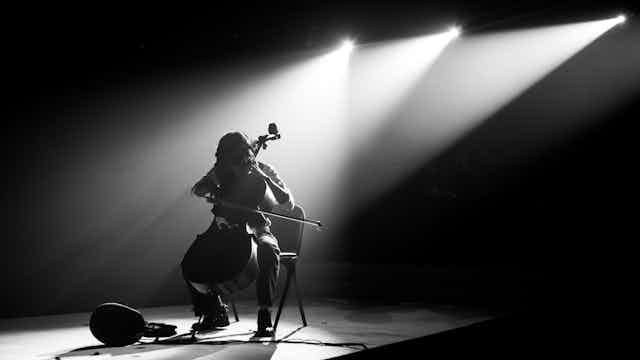 A cello player alone on stage, silhouetted by spotlights.